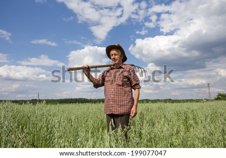 Tired old man farmer holding fork and looking at camera