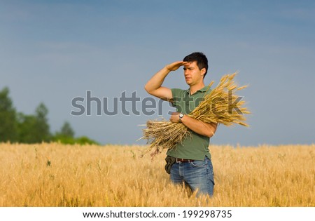 Attractive man with bunch of wheat in hands looking at his field