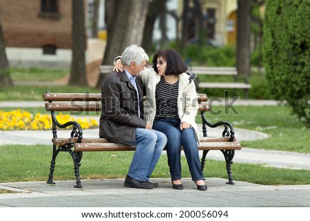 Older couple in hug sitting on bench in park