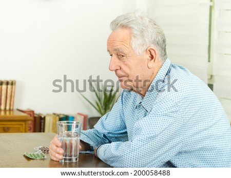 Old man in pajamas holding glass of water and have pills blister on table