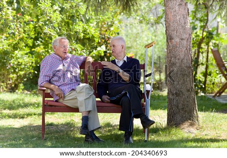 Two retired men sitting on bench in park and talking