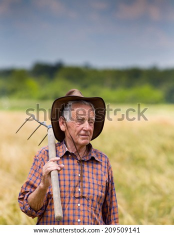 Proud old man farmer holding fork and looking at his field