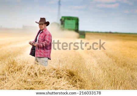Peasant holding tablet in wheat field with combine in background