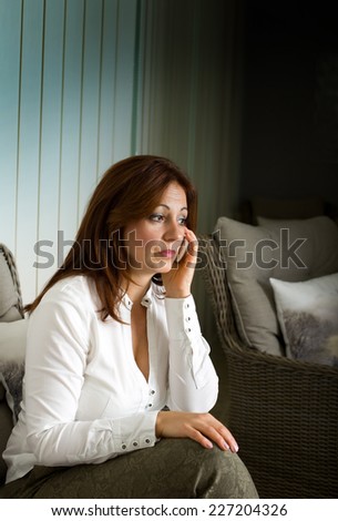 Worried middle aged woman talking on cell phone in living room