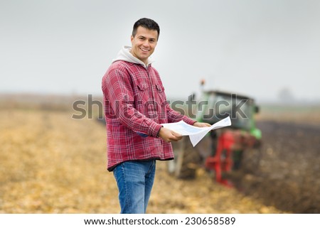 Happy young farmer with forms for bank loan standing on field, tractor in background