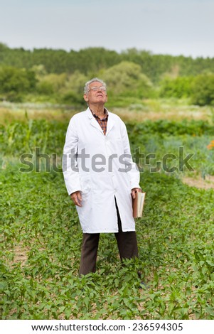 Old agronomist in white coat looking at sky for weather forecast