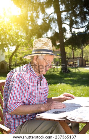 Old man reading newspapers in backyard at table
