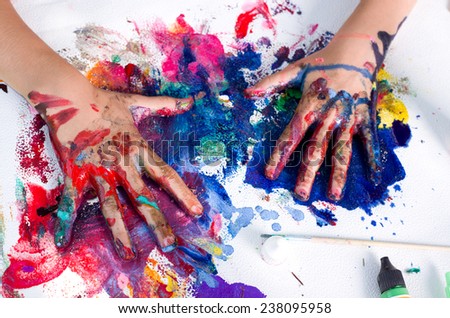 Painted hands smudging colors on messy paper
