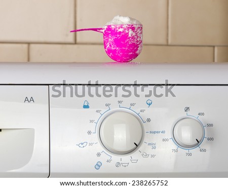 Pink plastic cup with washing powder on the top of washing machine in bathroom