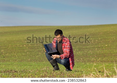 Young attractive peasant with laptop monitoring seedlings in the field
