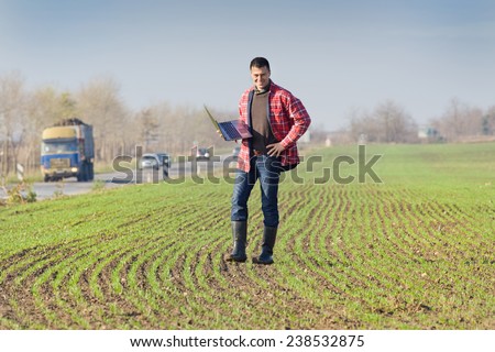 Young attractive peasant with laptop monitoring seedlings in the field