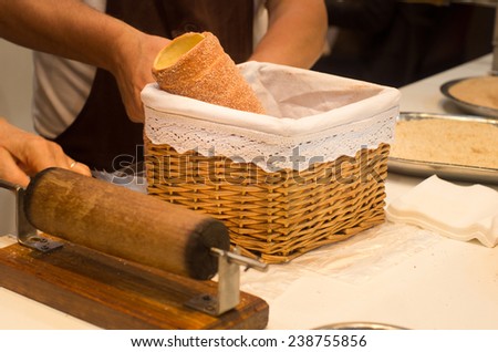 Chimney cake in decorated knitted basket on table with cook in background