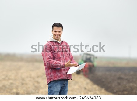 Happy young farmer standing on the field and showing good results on paper