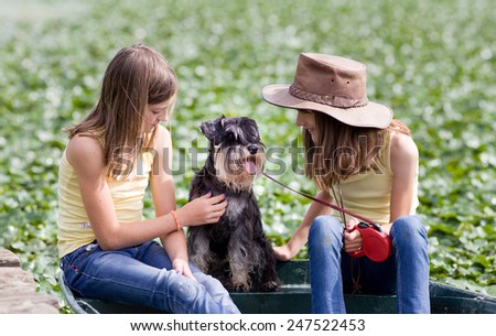Two young girls sitting on boat with their dog, green background with sun rays