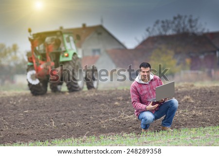 Young farmer with laptop on the field with seedlings in late autumn