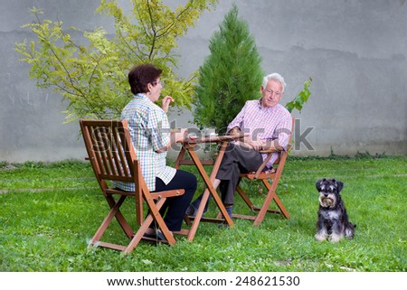 Senior couple with dog sitting in garden at table and having coffee and snack