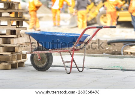 Dirty handcart standing on construction site, workers and machinery in background