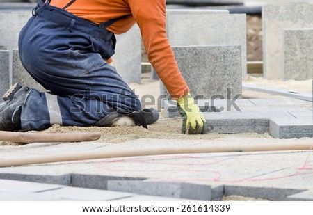 Construction worker on knees placing stone tiles in sand for pavement