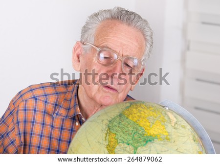 Close up of old man with reading glasses looking at globe