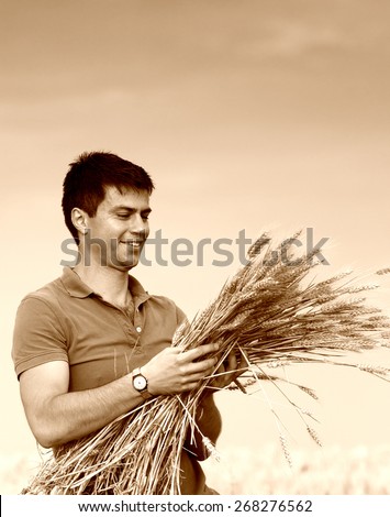 Satisfied young farmer holding bunch of ripe wheat, sepia image technique