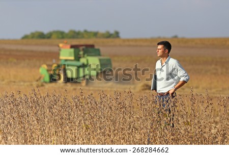 Conceived young businessman standing on soybean field during harvest