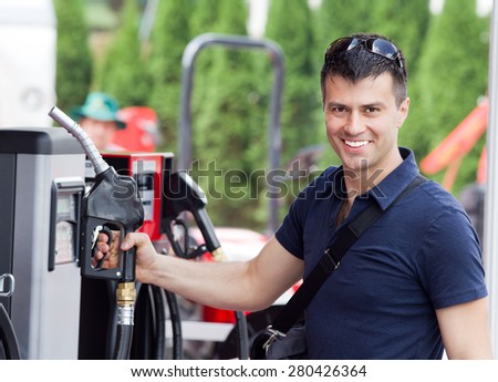 Happy young man holding fuel nozzle at gas station