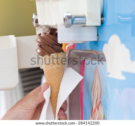 Human hand holding cone with twisted ice cream from machine
