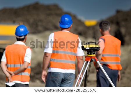 Theodolite on tripod at road construction site with workers supervising works