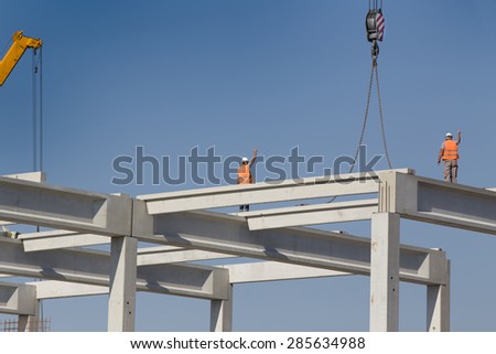 Construction workers standing on concrete beam on height and placing truss lifted by crane