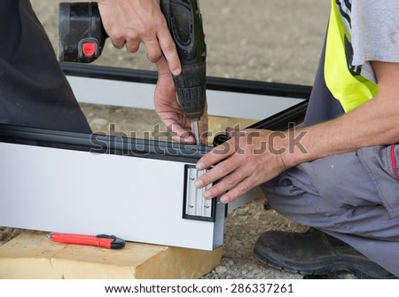 Two construction workers assembling metal profiles with screwdriver drill for ventilated facade on the ground at building site