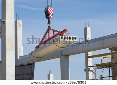 Concrete slab hanging from crane hook above building skeleton at construction site