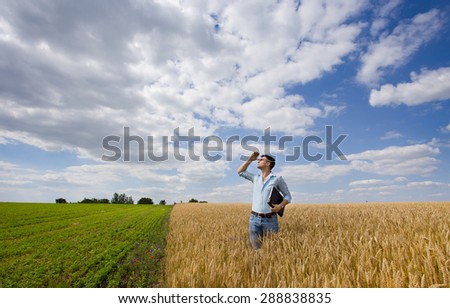 Young farmer standing in ripe wheat field and looking in the sky for rain