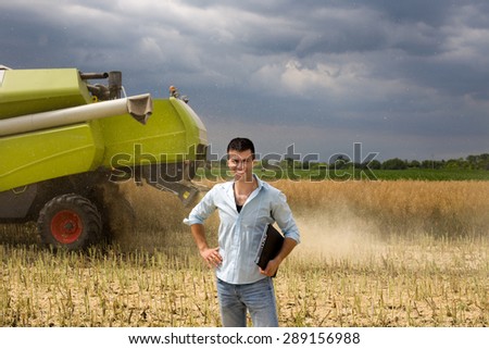 Young attractive farmer carrying laptop in the field during rapeseed harvest