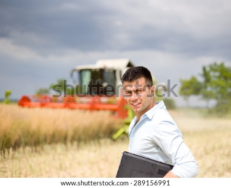 Young attractive farmer carrying laptop in the field during rapeseed harvest