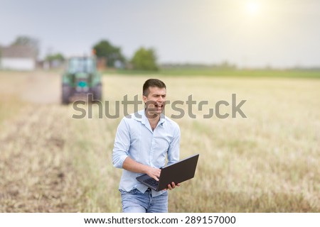 Young farmer with laptop trying to communicate by shouting because of noise at harvest in the field