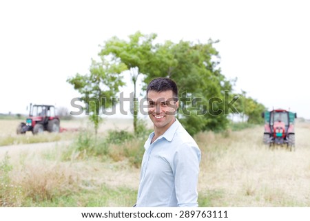 Young businessman standing in the field with two tractors in background