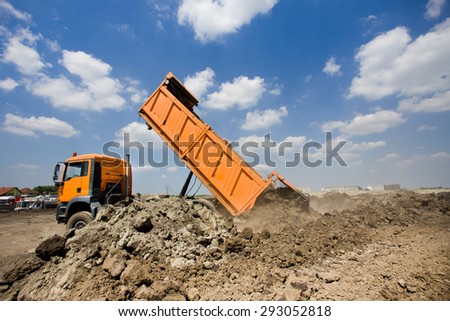 Orange truck tipping dirt on the construction site, blue sky with white clouds in background