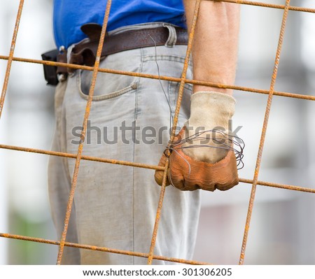 Close up of worker\'s hand with safety gloves carrying rusty reinforcement mesh
