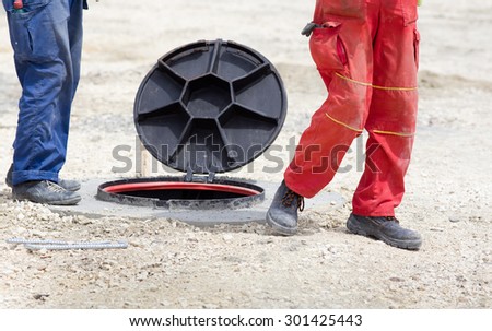 Construction workers standing beside manhole with open cover at building site