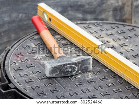 Close up of hammer and level standing on manhole cover at building site