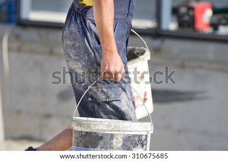 Construction worker in dirty work wear carrying two buckets with cement
