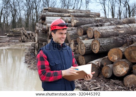 Young lumber engineer standing with notebook in front of cut trunk stock