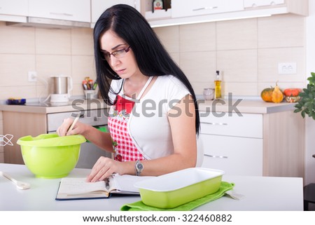 Young woman working in the kitchen, reading recipe for baking