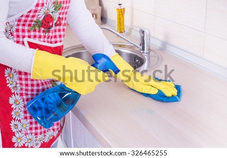 Young woman cleaning kitchen countertop with spraying detergent and rag