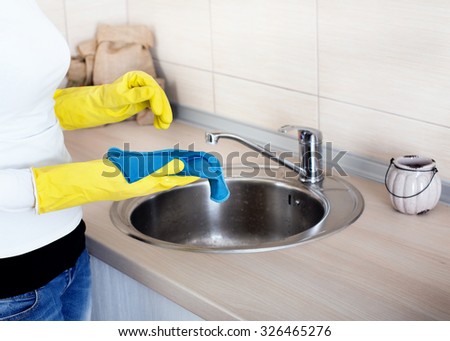 Close up of female hands with rubber gloves cleaning kitchen countertop and sink
