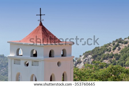 View of greek orthodox church belfry with cross on the roof. Rocky mountains and blue sky in background