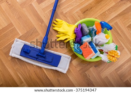 Top view of mopping stick and washbasin full of cleaning supplies and equipment on the parquet