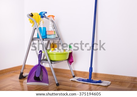 Cleaning supplies on ladder and mop and brush with dustpan on the parquet in the corner of room