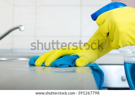 Close up of human hand in protective gloves holding mop and spray bottle and wiping kitchen countertop