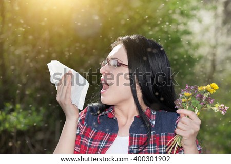 Young girl sneezing and holding paper tissue in one hand and flower bouquet in other. Allergies concept